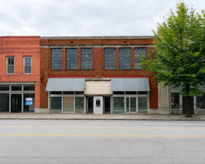Facade of red brick building with metal awnings, next to tree.