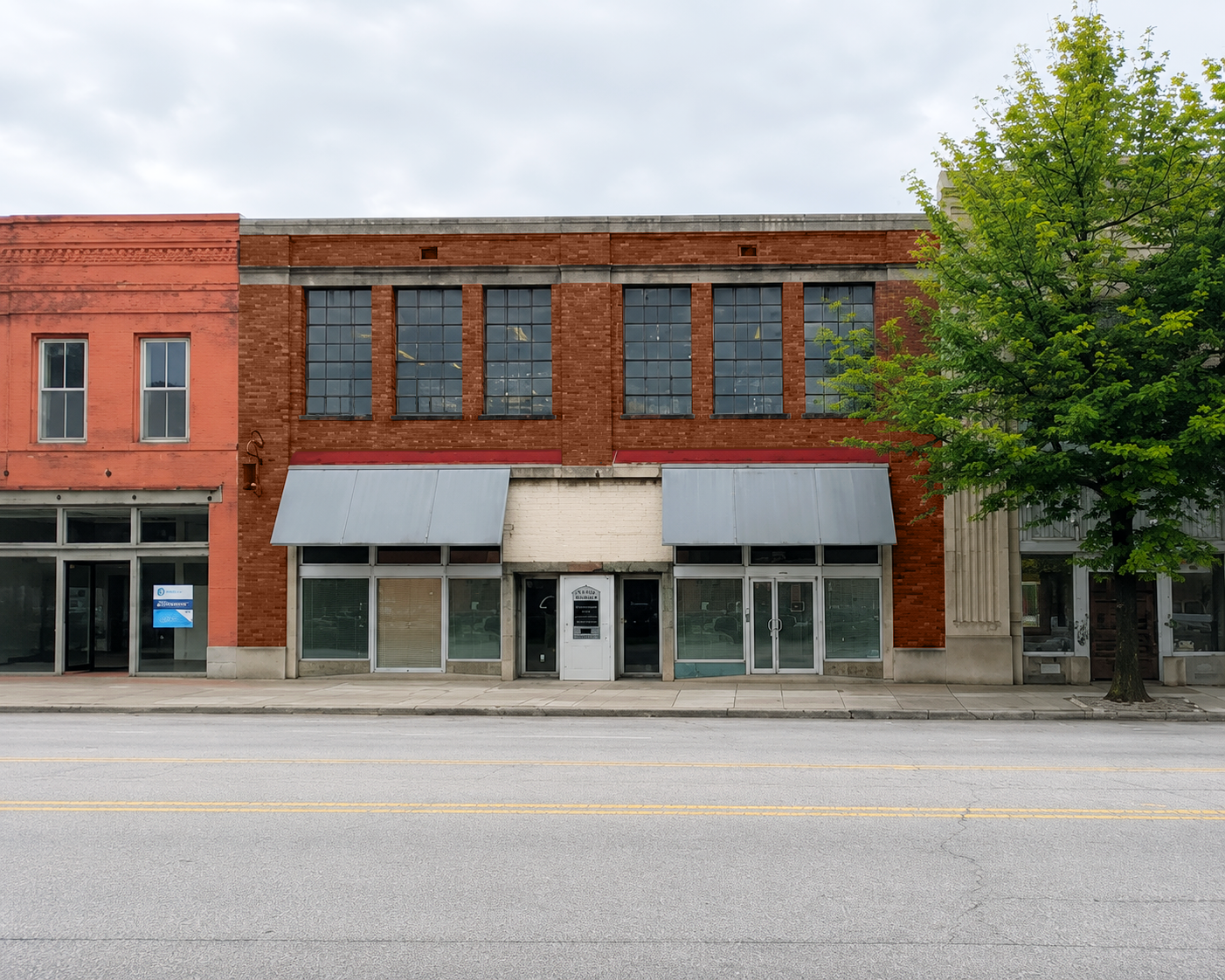 A brick building with metal awnings, next to a tree.