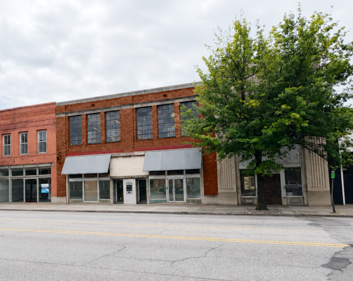 Facade of red brick building with metal awnings, next to tree.