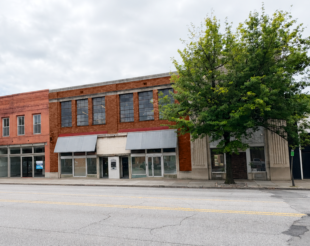 Facade of red brick building with metal awnings, next to tree.